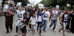 Eine kleinere Gruppe demonstriert und hält Schwarz-weiß-Fotos von Personen hoch