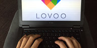 Zwei Frauenhände auf einer Laptoptastatur. Der Bildschirm zeigt das Logo der Datingplattform lovoo.