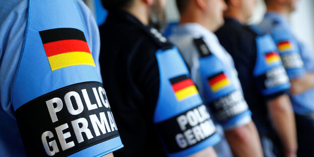 Die Oberarme mehrerer Polizisten, die hintereinander stehen, auf dem Ärmel der blauen eine Deutschlandfahne
