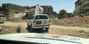 Ein Auto des Roten Kreuzes fährt durch eine zerstörte Stadt
