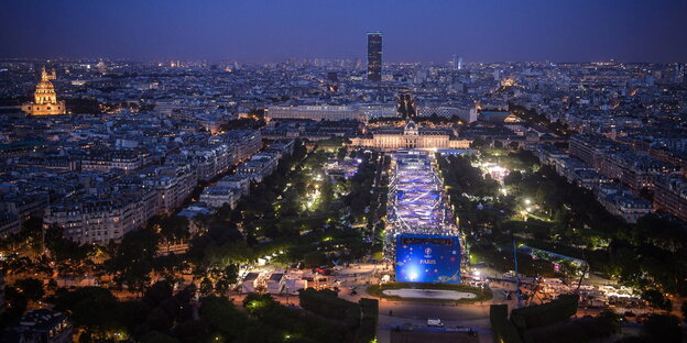 Luftaufnahme von Paris bei Nacht, links im Bild ist die hell erleuchtet Fanmeile