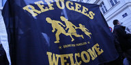 Eine dunkelblaue Flagge mit der gelben Aufschrift "Refugees Welcome"