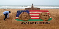 Ein Künstler an einer Sandburg mit den Gesichtern von Hillary Clinton und Donald Trump, der US-Flagge und dem Weißen Haus.