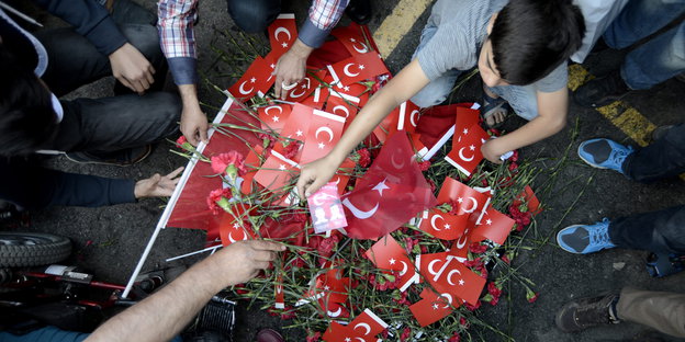 Ein Junge legt eine kleine türkische Flagge auf einen Haufen von weiteren türkischen Flaggen und roten Blumen.