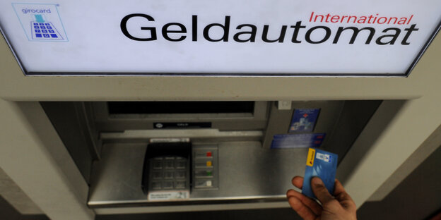 Eine Hand schiebt eine Karte in einen Geldautomaten