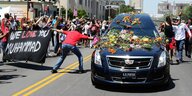 Menschen umringen einen mit Blumen bedeckten Leichenwagen bei der Trauerfeier für Muhammad Ali