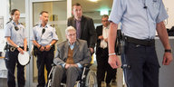 Der ehemalige SS-Wachmann Reinhold Hanning wird in einem Rollstuhl in einen Gerichtssaal geschoben, umgeben von Polizisten