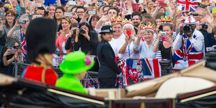 Queen Eilzabeth II. in einem froschgrünen Kostüm in einer Kutsche, dahinter jubelnde Menschen