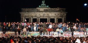 Es ist Nacht, vor dem Brandenburger Tor sitzen und stehen hunderte Menschen auf einer Mauer, weitere stehen davor.