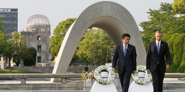 US-Präsident Barack Obama und der japanische Premierminister Shinzo Abe gehen nebeneinander, hinter ihnen liegen Blumenkränze vor einem Betonbogen.