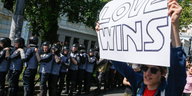 Ein mann mit einem Transparent „Love wins“, neben ihm sind viele Polizisten