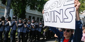Ein mann mit einem Transparent „Love wins“, neben ihm sind viele Polizisten
