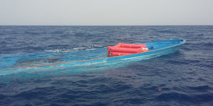 Ein Boot treibt knapp unter der Wasseroberfläche, darüber schwimmt eine rote Rettungshilfe