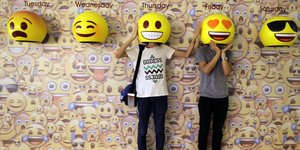 Zwei Menschen jeweils mit ihrem Kopf unter einer Emoji-Maske