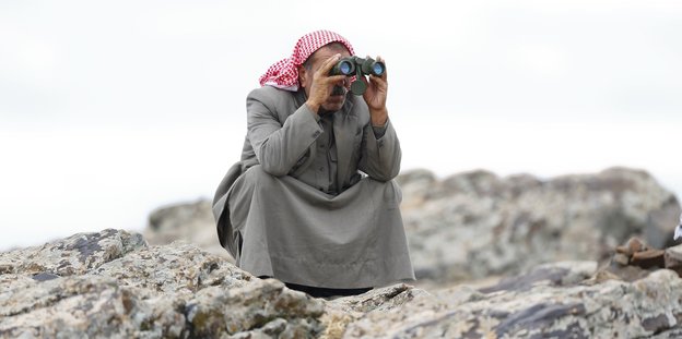 Ein türkischer Kurde hockt auf einem Felsen und schaut durch ein Fernglas