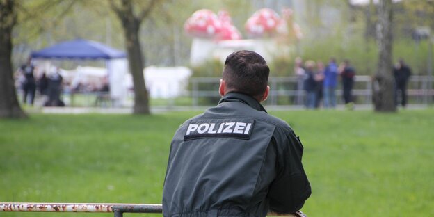 Ein Polizist lehnt auf einer Absperrung und beobachtet ein Rechtsrockkonzert in der Ferne