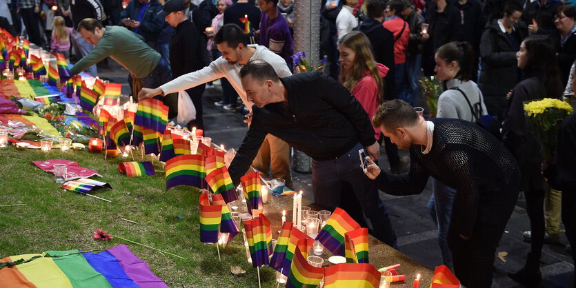 Blumen, Regenbogenflaggen und trauernde Menschen