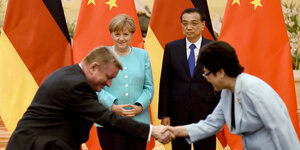 eine Frau und ein Mann schütteln sich die Hand, dahinter stehen Merkel und Ministerpräsident Li