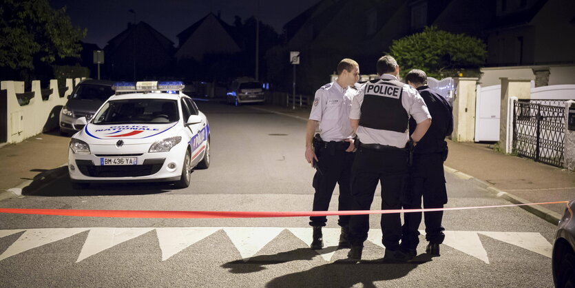 Drei Polizisten stehen neben einem Polizeiauto auf der abgesperrten Straße in Magnanville