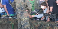 An einem Infostand hält ein Junge vor den Augen eines Soldaten ein Sturmgewehr