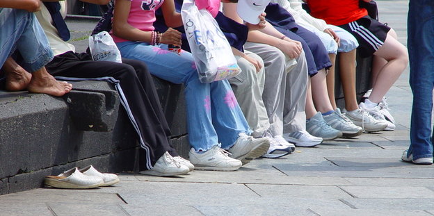 Kinder/Jugendliche sitzen auf einer Steinbank