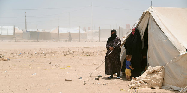 zwei Frauen und ein Kind stehen an einem Zelt in einer Wüste
