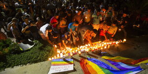 Viele Menschen zünden Kerzen an und stehen vor einer Regenbogen-Fahne