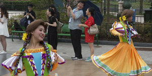 Tanzende Frauen in Kostümen. Im Hintergrund fotografieren Besucher mit Smartphones