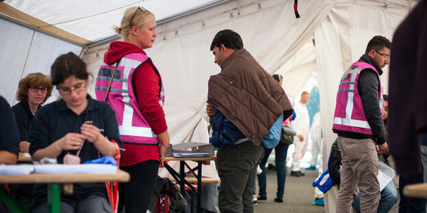 Helfer*innen und Asylsuchende stehen in einem großen weißen Zelt