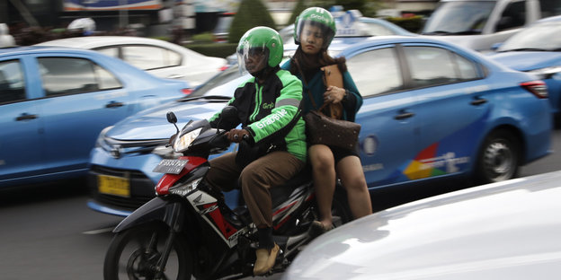 Ein Mann und eine Frau fahren auf einem Motorrad zwischen Autos