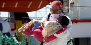 Ein Arzt trägt ein Kind von einem Schiff