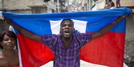 Ein Mann hält eine haitianische Flagge mit ausgebreiteten Armen hinter sich