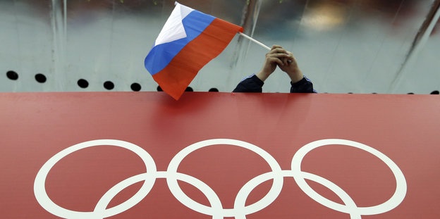 Zwei Hände halten eine russiche Fahne über dem Olympia-Logo