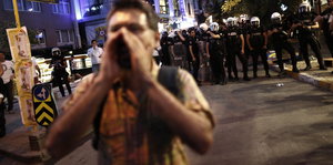 Im Hintergrund eine Polizeikette, im Vordergrund ein einzelner Demonstrant, der die Hände um den Mund legt und etwas ruft