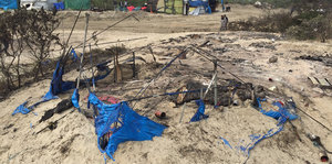 Auf einem Sandhügel liegen die Reste einer zerstörten Unterkunft: blaue Plastikfetzen und verkohlte Metallteile