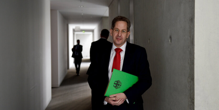 Hans-Georg Maaßen steht in einem halbdunklen Flur, hinter ihm bewegen sich dunkle Gestalten