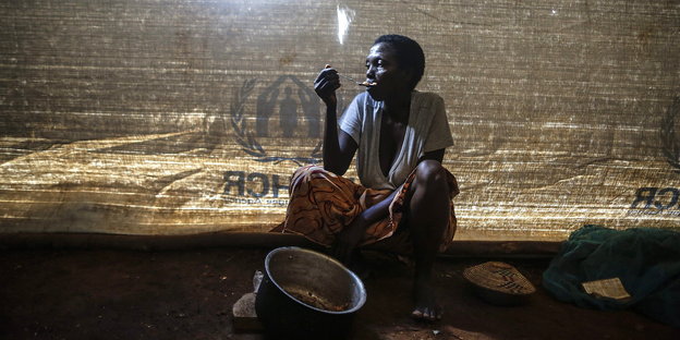 Eine Frau sitzt in einem Zelt, auf dem UNHCR zu lesen ist, und isst.