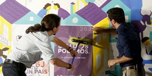 Zwei Männer kleben gemeinsam Plakate an die Wand, links zu sehen: der Podemos-Chef Pablo Iglesias