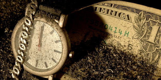 Eine alte Armbanduhr liegt neben einem Scheck im Staub