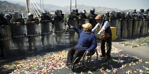 Ein Mann im Rollstuhl vor Polizisten mit Schilden und Kampfmontur