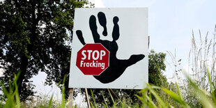 eine grüne Wiese, darauf ein Schild mit einer Hand und einem Stopp-Zeichen, auf dem „Stop Fracking“ steht