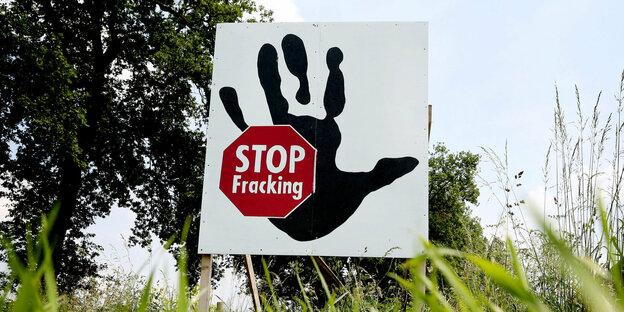 eine grüne Wiese, darauf ein Schild mit einer Hand und einem Stopp-Zeichen, auf dem „Stop Fracking“ steht