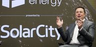 Elon Musk sitzend, vor dem Firmenlogo von SolarCity