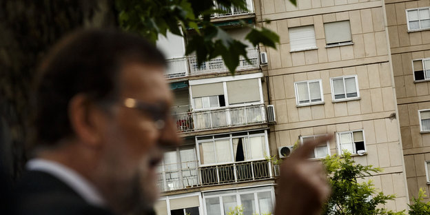 Mariano Rajoy steht mit erhobenem Zeigefinger vor einem Mehrfamilienhaus