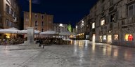 Städtischer Platz mit Restauranttischen bei Nacht