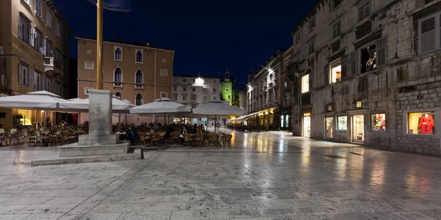 Städtischer Platz mit Restauranttischen bei Nacht