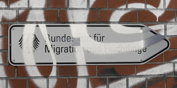 Auf einem Schild steht: "Bundesamt für MIgration und Flüchtlinge", darüber Graffiti