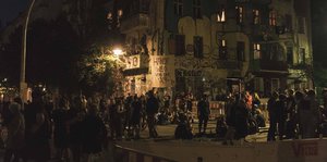 Menschen stehen bei Nacht vor einem Hausprojekt, zwischen Sperrzäunen