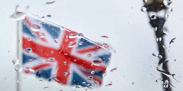 Durch eine verregnete Glasscheibe ist eine britische Flagge und eine Straßenlaterne zu sehen