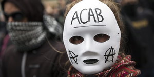 ein Mensch trägt eine Maske mit der Aufschrift ACAB auf der Stirn